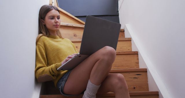 Caucasian woman sitting on stairs and using laptop at home. Communication, relaxation, lifestyle and domestic life, unaltered.