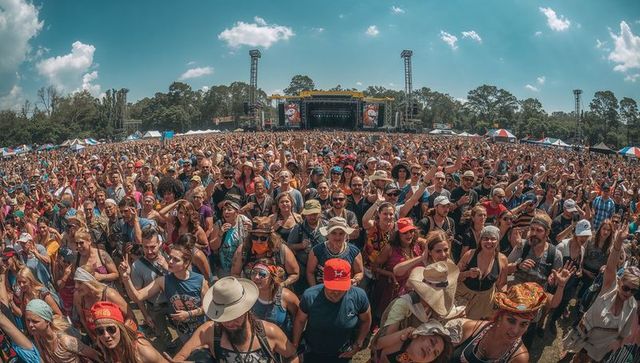 Crowd cheering and waving at outdoor summer music festival stage with hats and sunglasses