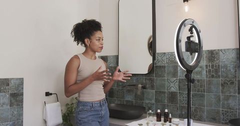 African american beauty creator filming skincare tutorial at vanity with ring light