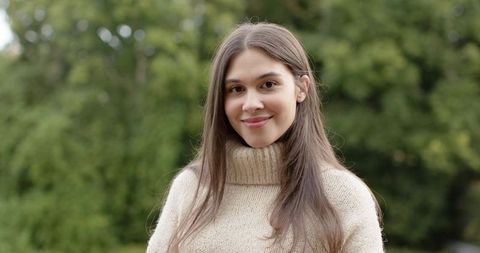 Young woman smiling outdoors in cream knit turtleneck portrait with green bokeh background