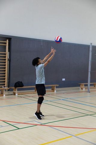 African american teen jumping reaching for volleyball on indoor gym court