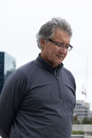 Thoughtful senior man standing in urban plaza wearing dark zip pullover and glasses