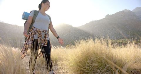Woman Hiking Through Tall Grass at Sunrise in Mountain Landscape
