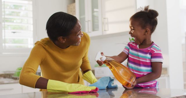Mother and young daughter happily cleaning kitchen together, creating bond while participating in household chores. Ideal for themes of family bonding, parenting, teamwork, responsibility, and joyful moments in everyday life. Suitable for use in parenting magazines, household cleaning product ads, and family-related articles or blogs.