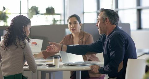 Multicultural team collaborating around laptop during office meeting chart presentation