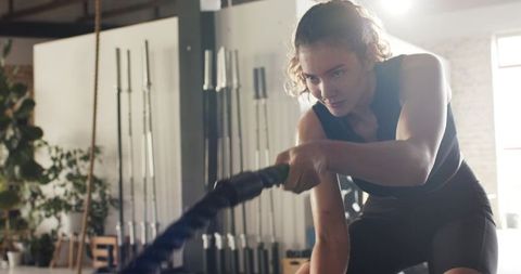 Athletic woman training with battle rope in gym