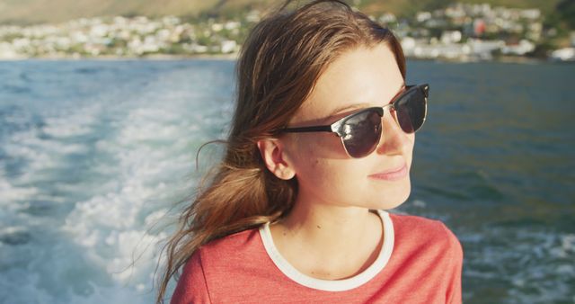 Smiling caucasian teenage girl in sunglasses out on deck of small boat sailing on a sunny day. Leisure, hobbies, free time, travel and vacations.