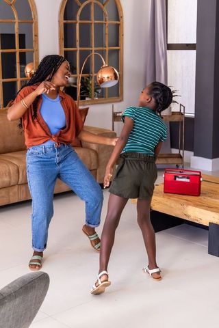 Joyful black mother and daughter dancing in warm modern living room with retro red radio