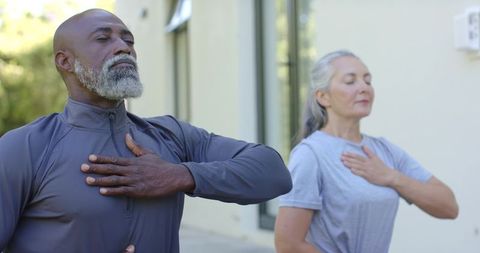 Mature diverse couple practicing deep breathing outdoors for mindfulness and wellness