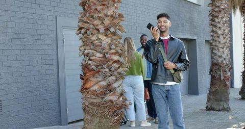 Young diverse friends chatting on sunny urban sidewalk with palm trees and casual fashion