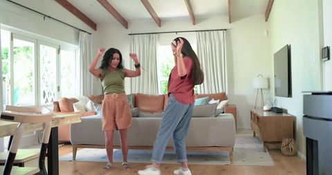 Two friends dancing and laughing in cozy modern living room with sofa and natural light