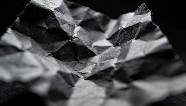 Crumpled black paper macro texture with sharp creases, torn edge, dramatic lighting