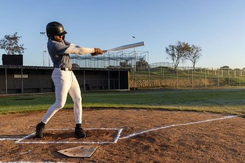 Right-handed batter swinging at incoming pitch on sunrise baseball field home plate