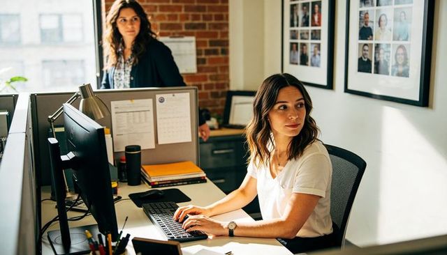 Young professional typing at desk while turning to colleague in bright modern office