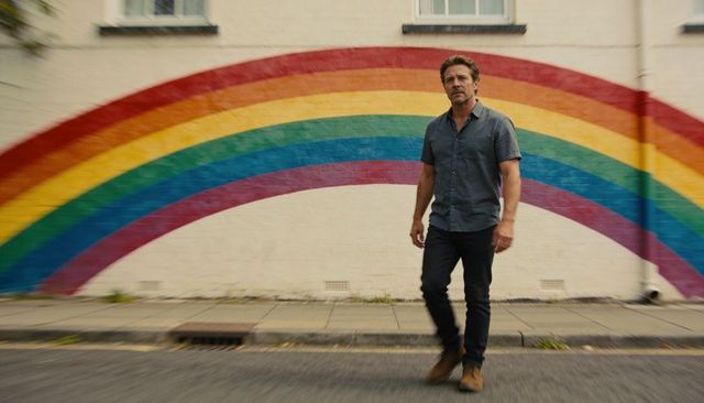 Man walking past rainbow mural on urban wall sidewalk casual style pride concept