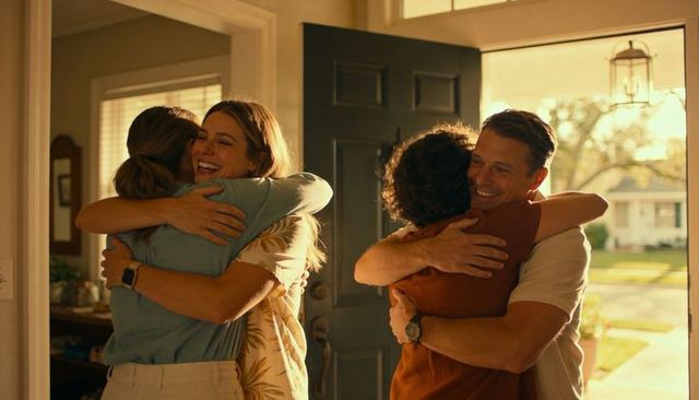 Sunlit homecoming embrace: four adults reuniting at open front door, warm porch welcome