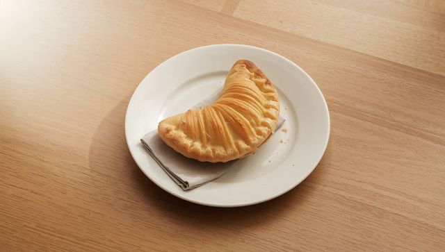 Golden crescent pastry sitting on white plate with linen napkin on wood table