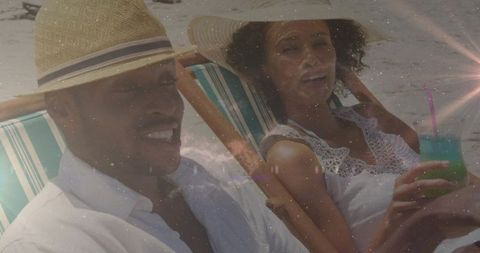 Couple relaxing on beach chairs wearing straw hats and sipping tropical green cocktail