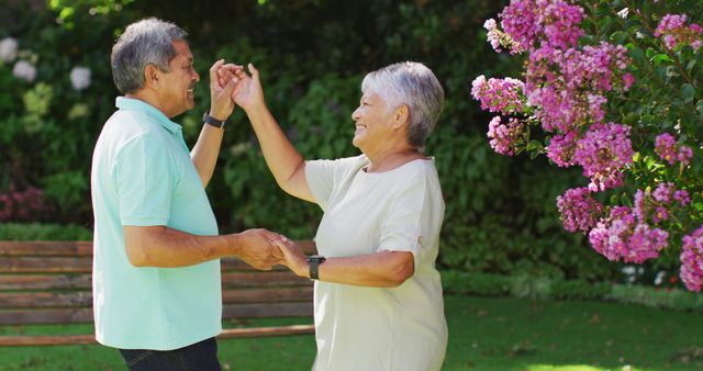 Happy senior couple dancing joyfully together in a lush garden. An elderly man and woman smile and hold hands surrounded by greenery and blooming flowers. Perfect for concepts related to happy aging, romance in elderly years, healthy and active retirement, and spending quality time outdoors.
