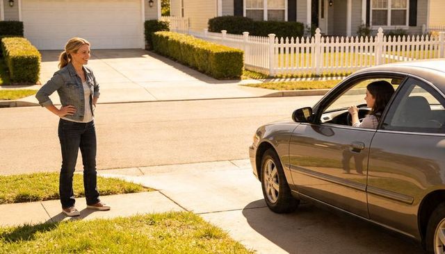 Smiling woman talking with teen driver on driveway in sunny suburban neighborhood