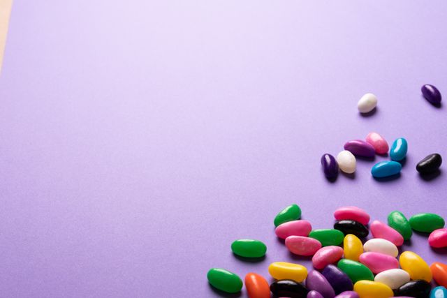 This image features a variety of colorful jelly beans scattered on a purple background. Ideal for use in advertisements for candy, party invitations, children's events, or any content related to sweets and desserts. The vibrant colors and playful arrangement make it perfect for adding a fun and cheerful touch to marketing materials or social media posts.
