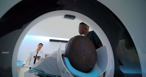 Mri team positioning african american patient in head scanner while doctor consulting tablet