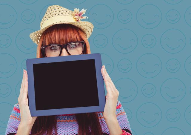 Digital composite of Woman straw hat with tablet over face against blue emoji pattern