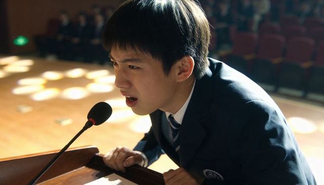 Determined high school student delivering speech at lectern under auditorium spotlight