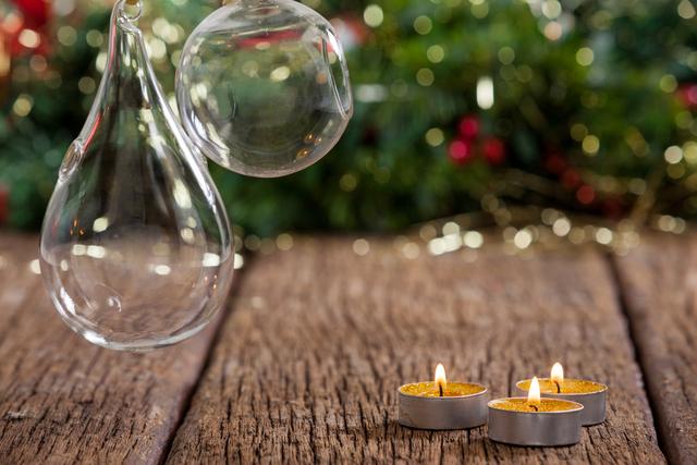 Tealight candles glowing on a rustic wooden plank with blurred Christmas decorations in the background. Ideal for holiday greeting cards, festive invitations, seasonal blog posts, and cozy home decor inspiration.