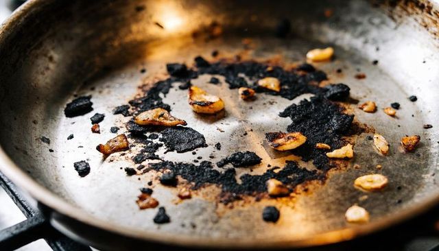 Burnt garlic and charred residue in stainless-steel skillet showing heavy carbon buildup