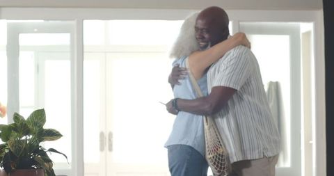 Senior Man Hugging Daughter at Home Entrance with Tote and Smartphone