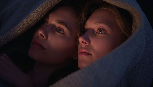 Two women cuddling under blanket looking up warm evening light intimate cozy closeup