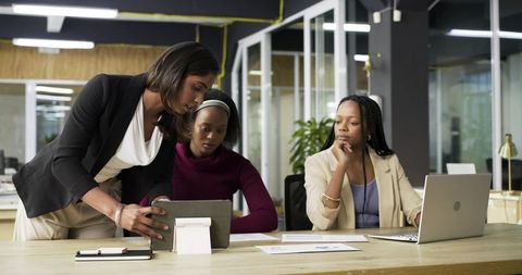 Diverse businesswomen collaborating over tablet and charts in modern open-plan office