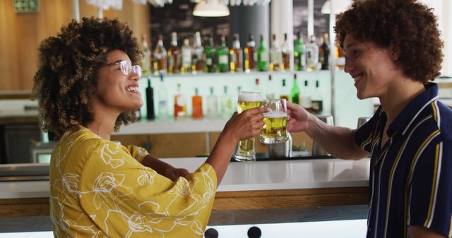 A vibrant scene featuring young adults clinking glasses of beer while smiling and enjoying time at a lively bar. Ideal for social life promotions, articles about nightlife, advertising for bars or restaurants, and banners for events.