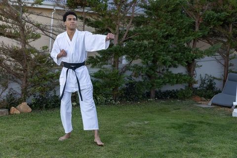 Young african american black belt practicing karate on backyard lawn, focused training
