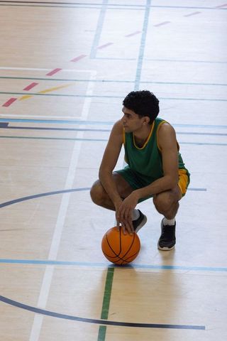 Youth Basketball Player Crouching with Ball in Gymnasium