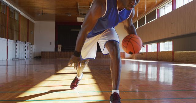 African american male basketball player practicing dribbling ball. basketball, sports training at an indoor court.