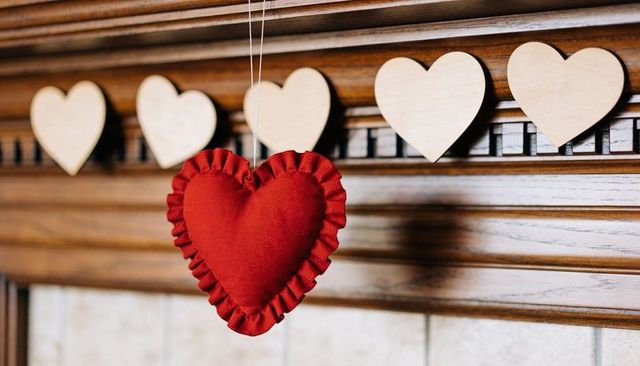 Red ruffled heart ornament hanging on wooden mantel with pale wooden heart garland
