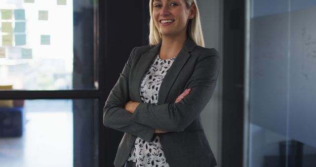 This image depicts a confident Caucasian businesswoman smiling with arms crossed, ideal for use in corporate materials, leadership articles, business websites, and marketing collateral. The professional and approachable demeanor can enhance profiles, promote female leadership, or illustrate success in business environments.