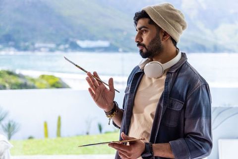 Painting on waterfront terrace with headphones and palette, contemplative artist