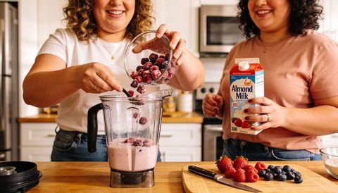 Two women blending berry smoothie with almond milk in bright home kitchen