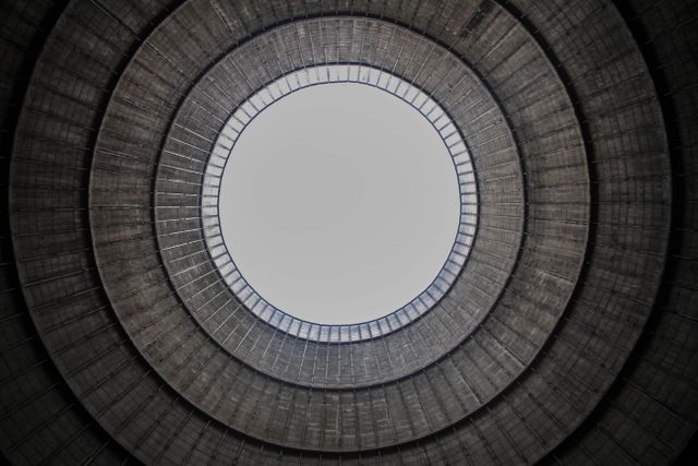 An abstract view of a circular industrial structure with a symmetrical pattern and minimalist design elements. The concentric rings create a dramatic and visually appealing effect, showcasing a mix of concrete textures and modern construction techniques. Ideal for use in architectural magazines, design inspirations, urban landscape studies, and modern art concepts.