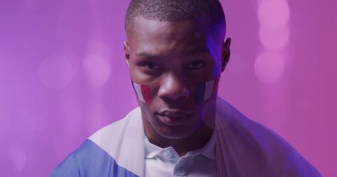 Young Male Sports Fan with French Flags Painted on Face Against Pink Backdrop