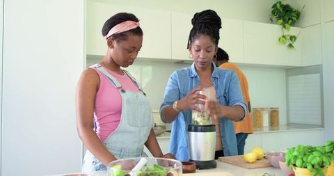 African american family making healthy smoothie on kitchen island, mother using blender
