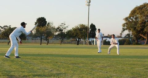 Sunlit amateur cricket match batting and fielding on green parkland during golden hour