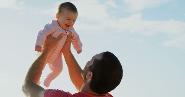 Caucasian father holding happy baby above his head against sunny blue sky, copy space. Fatherhood, care, wellbeing, vacations, nature and travel, unaltered.