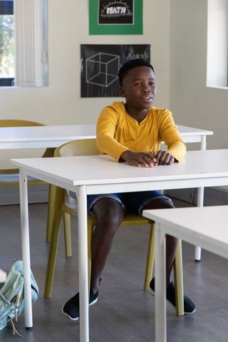 African american boy sitting at classroom desk wearing mustard shirt and learning