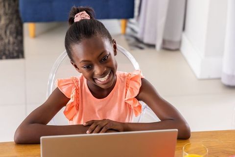 Smiling african american girl using laptop for online learning at home with orange juice