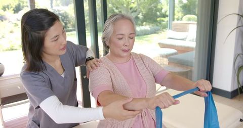 Physical Therapist Assisting Senior Woman with Exercise Band at Home