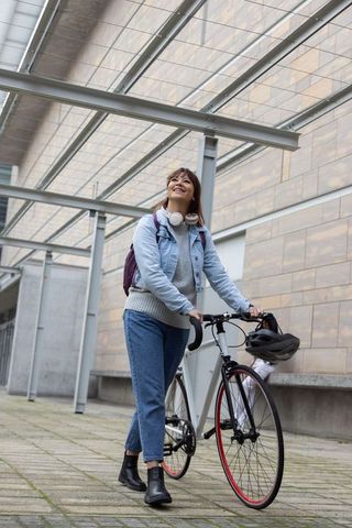 Young woman walking road bike under glass canopy, looking up and smiling — urban commuter